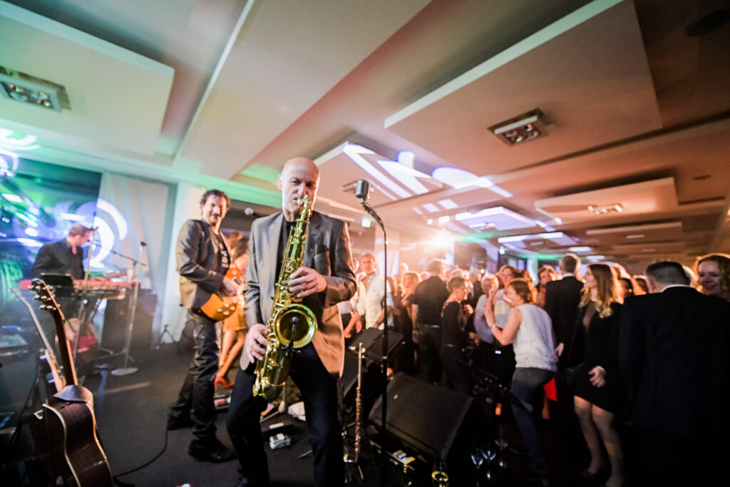 Partybild aufgenommen aufunserer großen Tastetival Wein und Genussparty im Foyer vor den Veranstaltungsräumen D1-D3 im Vordergrund eine Band auf der Bühne zu sehen im Hintergrund eine Menschenmenge beim Tanzen