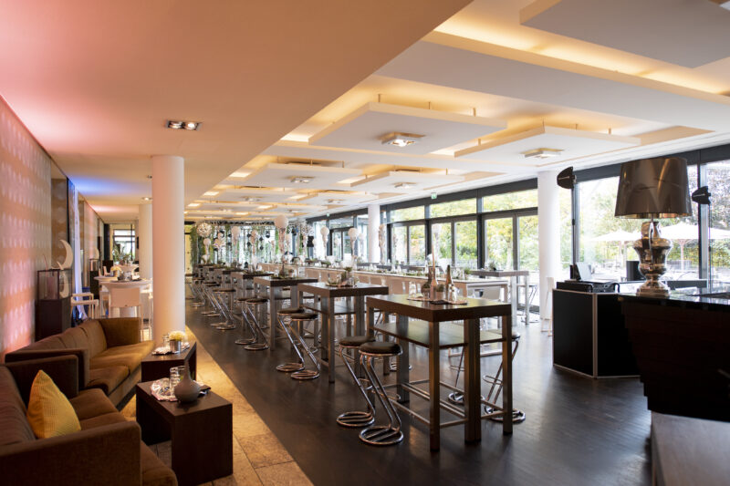 Foto bei Tageslicht aufgenommen des Foyers vor den Veranstaltungsräumen D1, D2 und D3 zu sehen die Partybestuhlung für die anstehende Tastetival Wein und Genussparty am Abend. Hochtische und Hochstühle im gesamten Foyerbereich verteilt