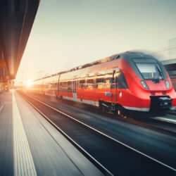 Schöner Bahnhof mit modernem rotem Hochgeschwindigkeits-Pendelzug mit Bewegungsunschärfe-Effekt bei buntem Sonnenuntergang in Nürnberg, Deutschland. Eisenbahn mit Vintage Tonung
