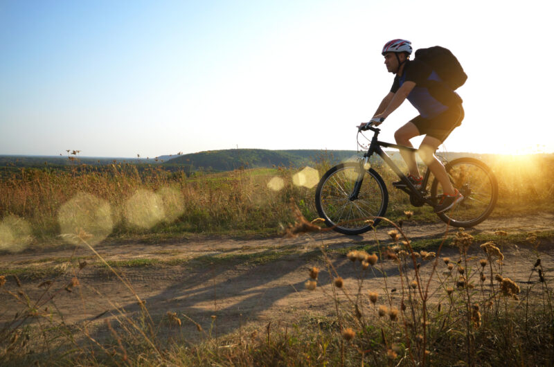 Männlicher Radfahrer mit Rucksack auf einem ländlichen Feldweg im Freien