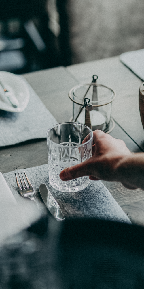 Servicemitarbeiter ist beim Eindecken des Restaurant Tisches und deckt gerade das Wasserglas ein, man sieht nur seine Hand