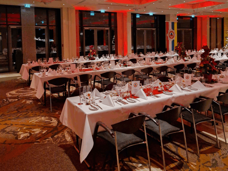 Veranstaltungsraum E1, E2 und E3 kombiniert, in einer Tafelbestuhlung für 250 Personen am Abend fotografiert, die Decke und die Säulen am Rand sind leicht rot angestrahlt im Hintergrund zu sehen ein geschmückter Weihnachtsbaum