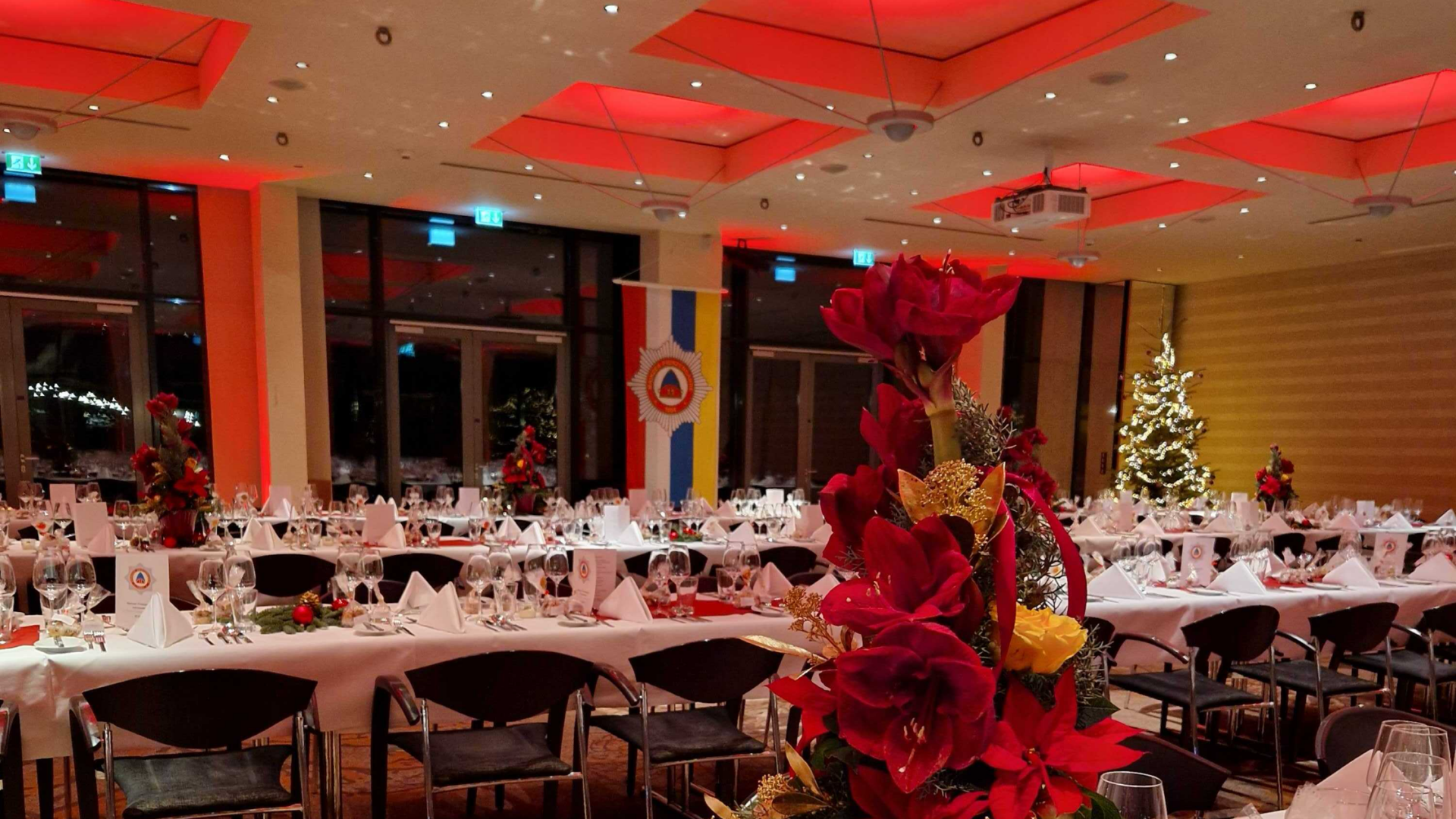 Veranstaltungsraum E1, E2 und E3 kombiniert, in einer Tafelbestuhlung für 250 Personen am Abend fotografiert, die Decke und die Säulen am Rand sind leicht rot angestrahlt im Hintergrund zu sehen ein geschmückter Weihnachtsbaum