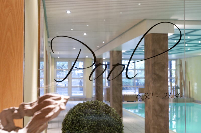 Schriftzug Pool auf unserer Glasscheibe vor dem Eingang zum Pool