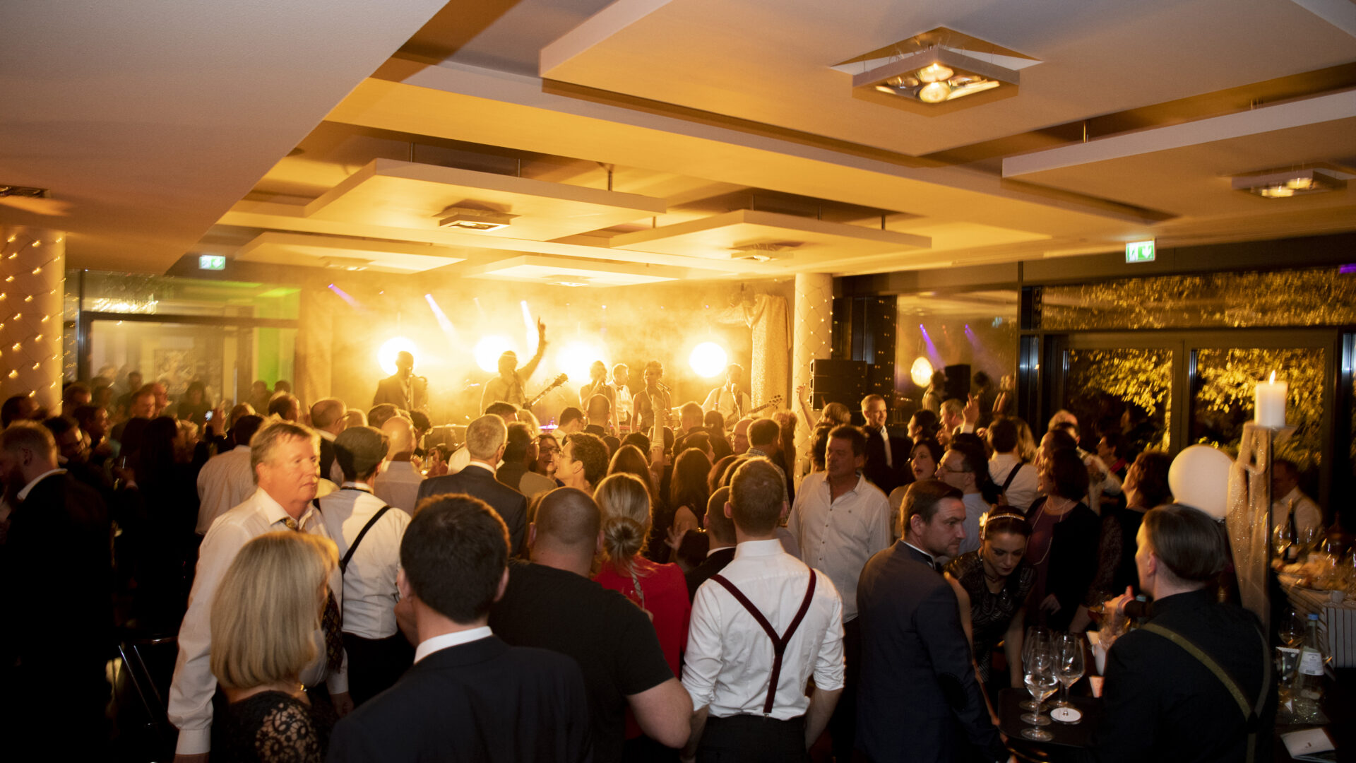Partybild aufgenommen aufunserer großen Tastetival Wein und Genussparty im Foyer vor den Veranstaltungsräumen D1-D3 im Hintergrund eine Band auf der Bühne zu sehen im Vordergrund eine Menschenmenge beim Tanzen